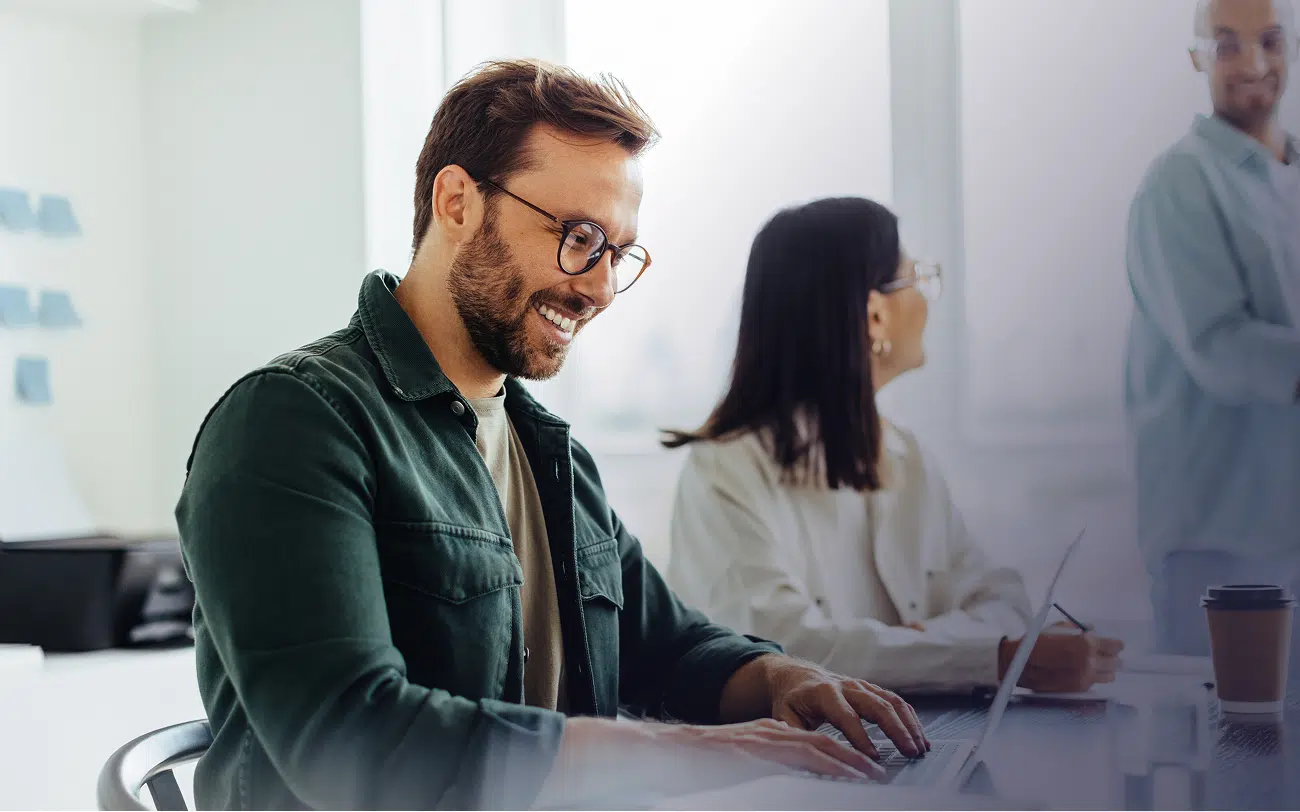 A man in a green shirt and glasses is typing on his laptop, concentrating on his task.